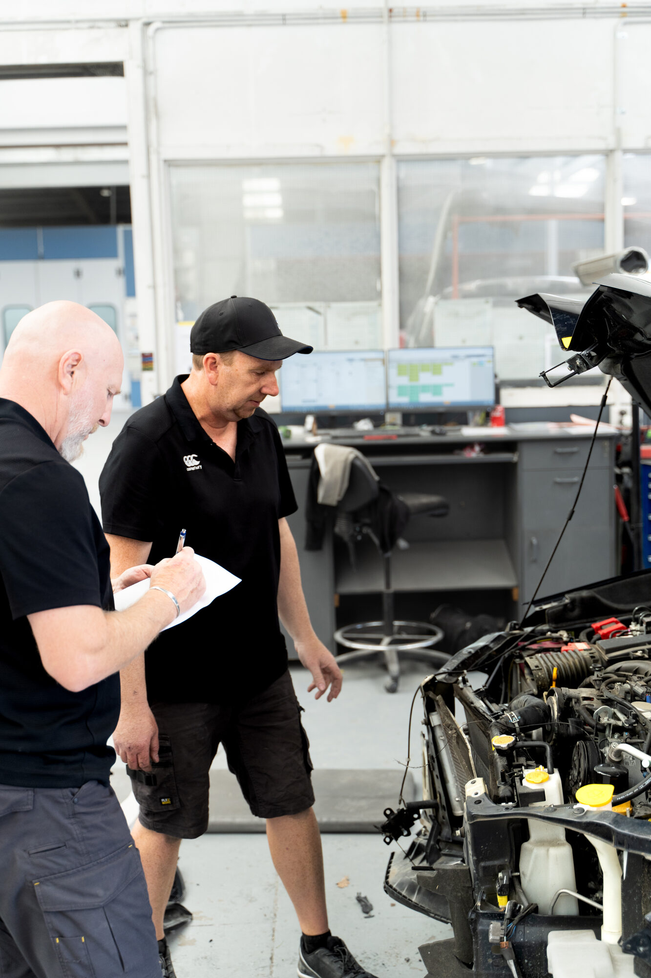 Two Avon City Paint & Panel staff assessing a stripped-down vehicle in the Sockburn workshop